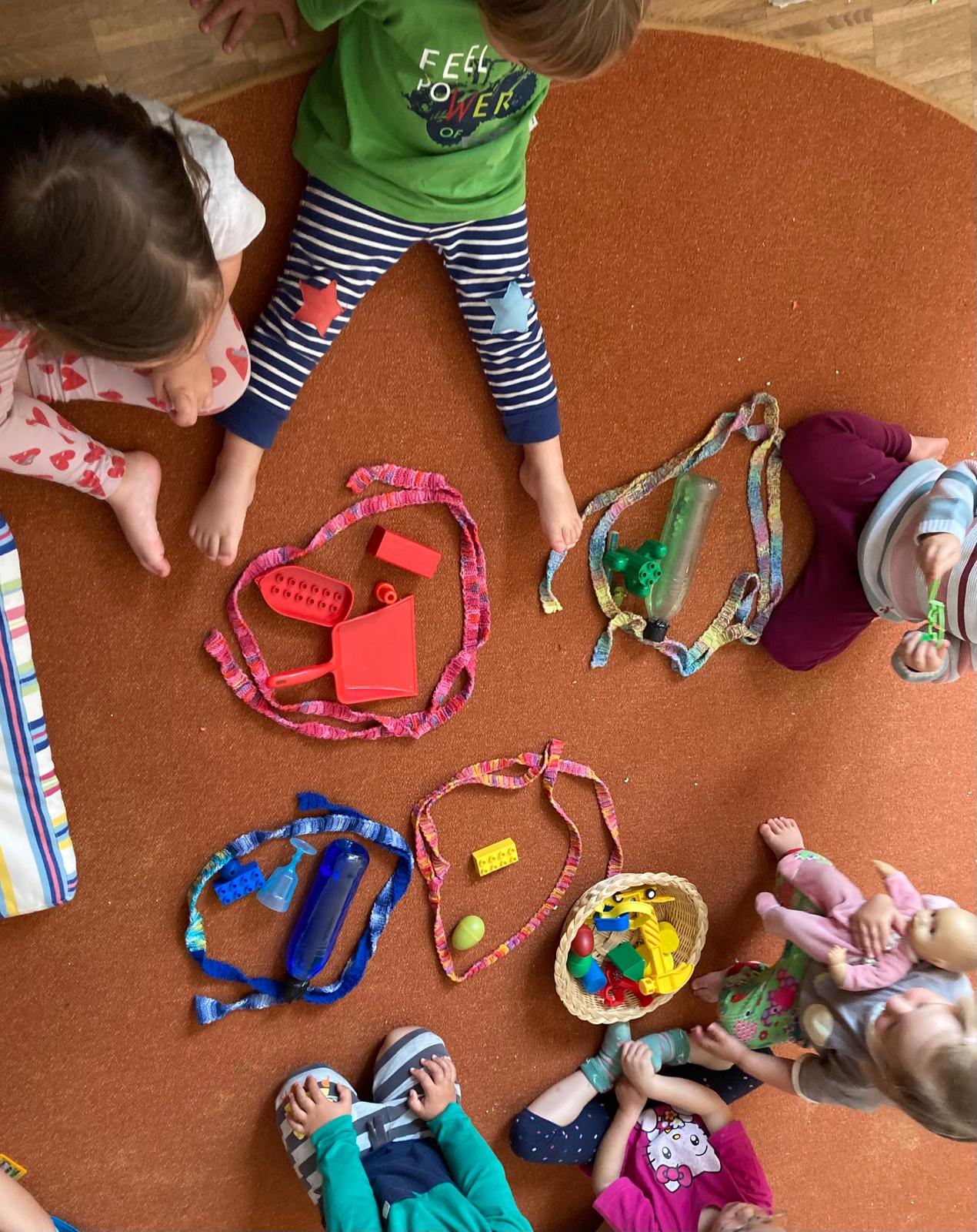 Kleinkinderbetreuung Buchloe - Kinder sitzen auf einem Teppich und sortieren Spielzeug nach Farben